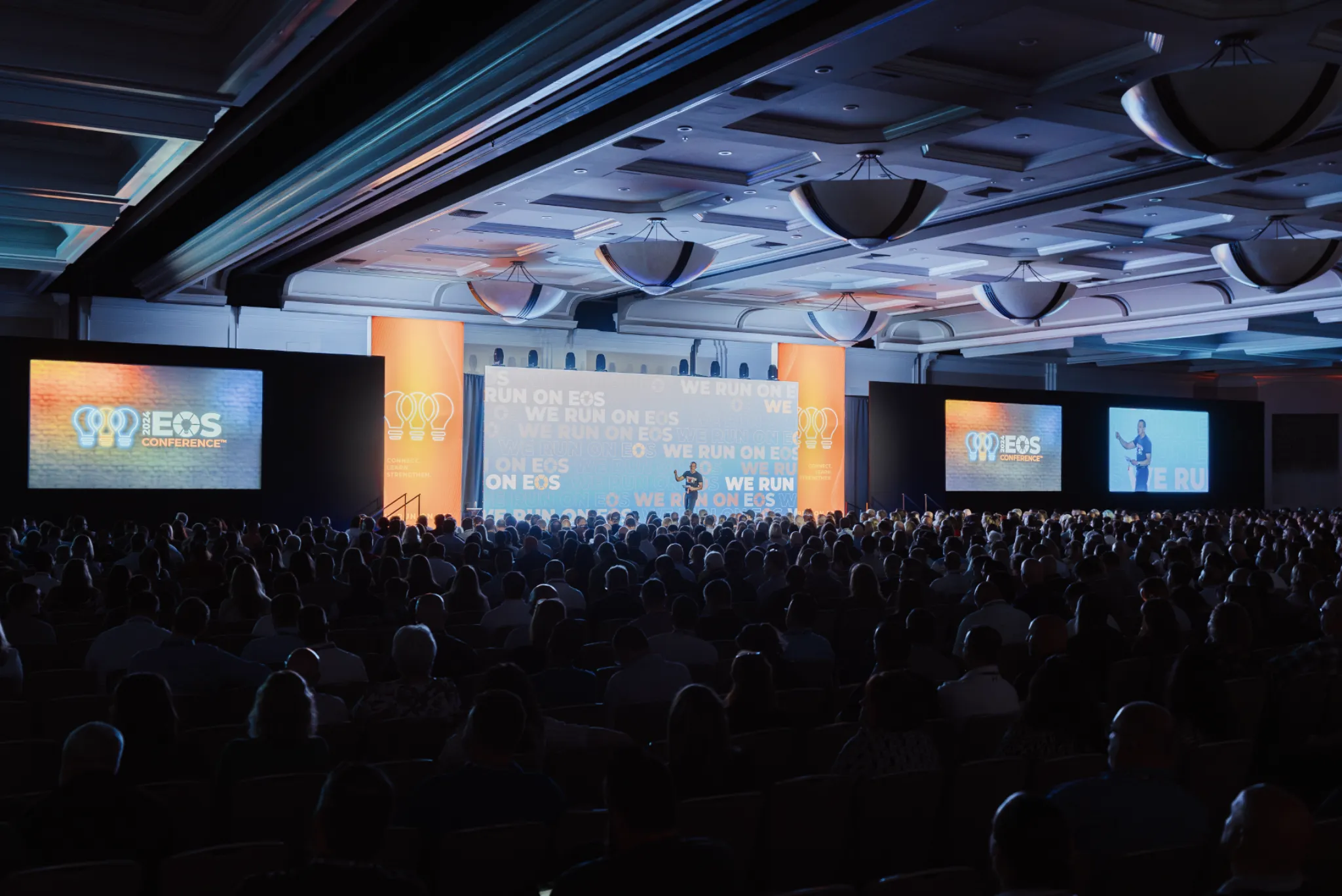 EOS User Conference ballroom packed with attendees facing a stage with LED screens reading ‘We Run on EOS’
