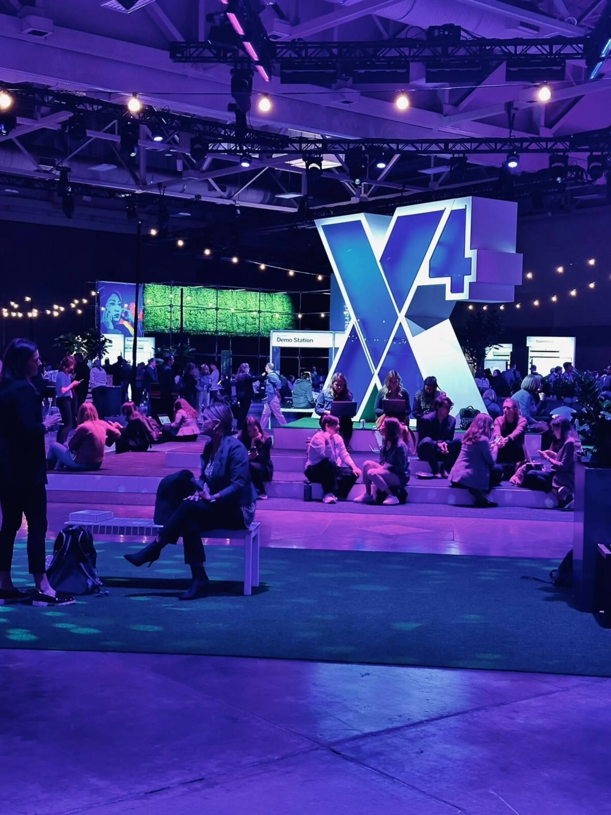 Attendees relaxing around the X4 letter sculpture inside the main convention hall with purple stage lighting