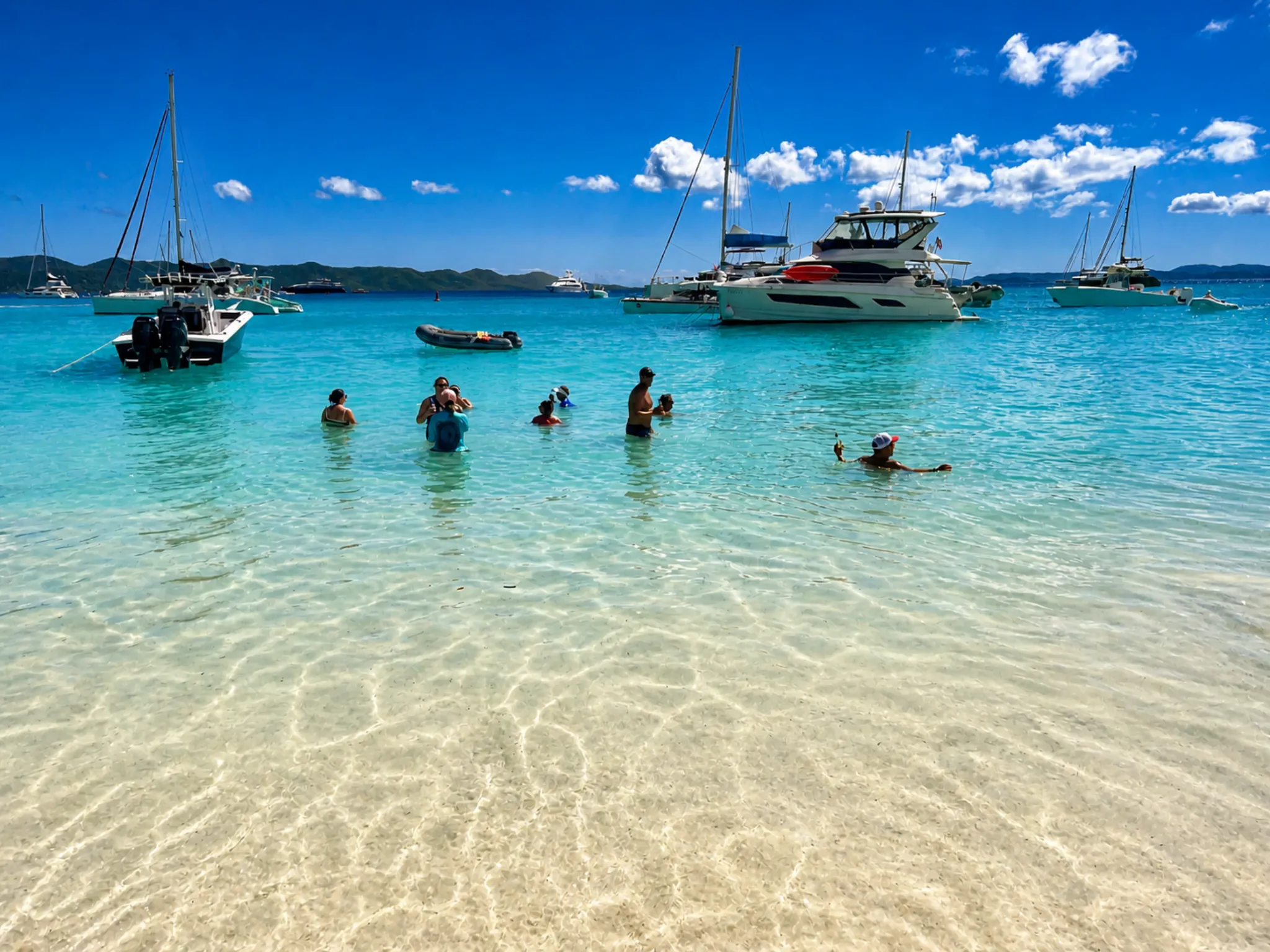 Reach for the Beach attendees swimming in turquoise Caribbean water with luxury catamarans moored in the bay