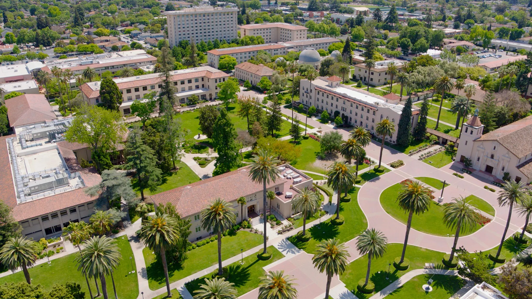 Aerial view of Santa Clara University campus with palm trees, red-tile rooftops and manicured courtyard gardens