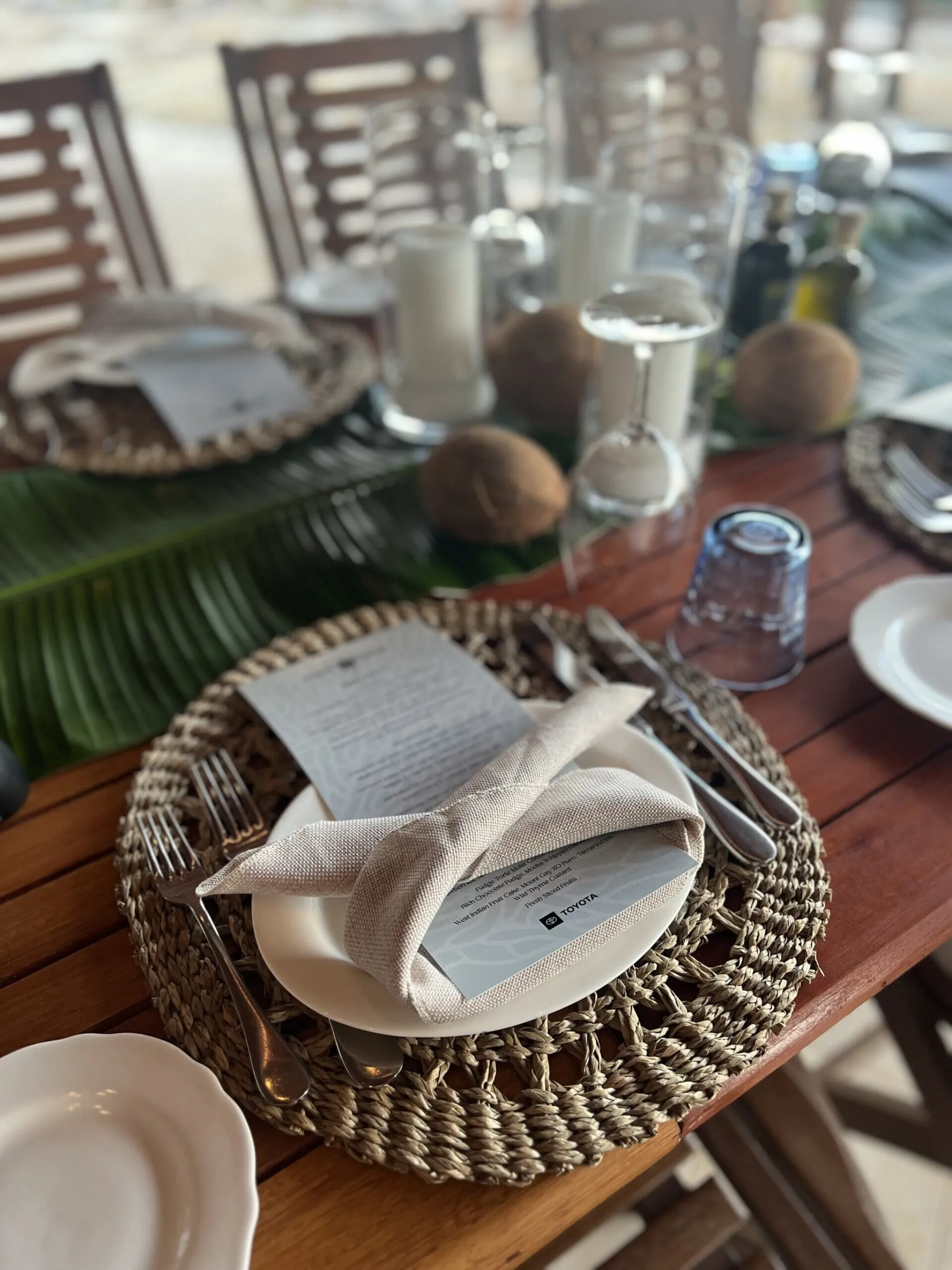 Curated Toyota-branded place setting with woven charger, tropical greenery, and a printed menu card