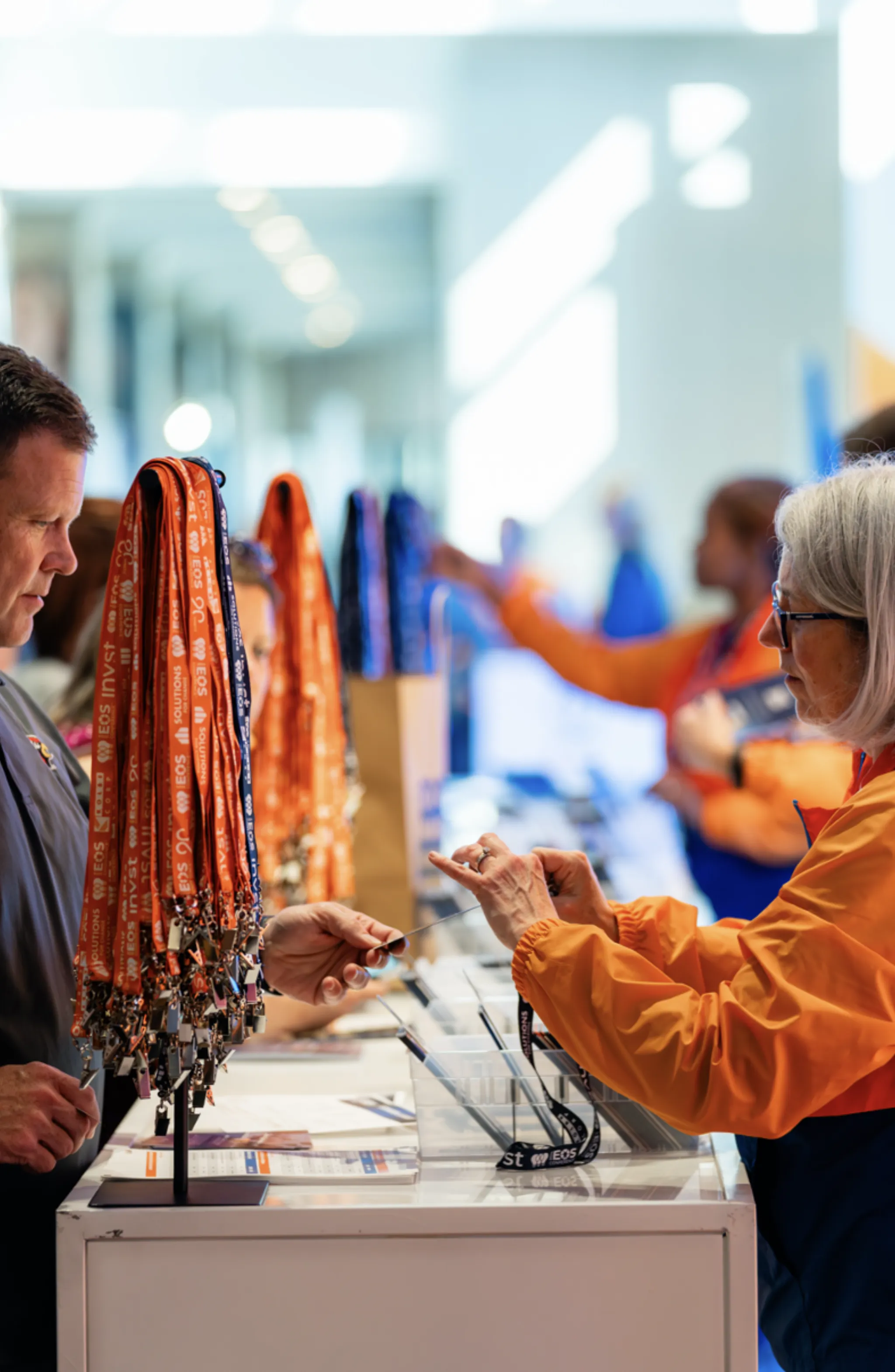 Attendee browsing branded EOS lanyards on a display rack at the conference registration counter