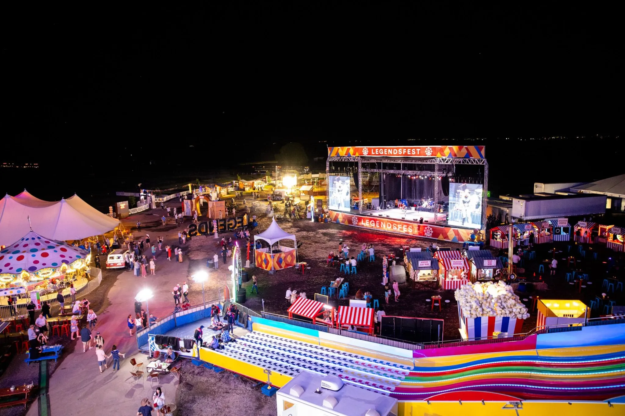 Aerial view of the LegendsFest grounds at night with stages, tents, and attractions